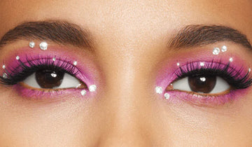 A close up of a woman's eyes with pink eyeshadow and face gems surrounding the eyes. 