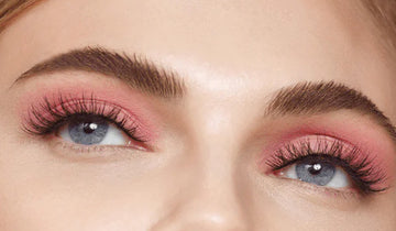 A close up of a woman with pink eyeshadow and long eyelashes. 