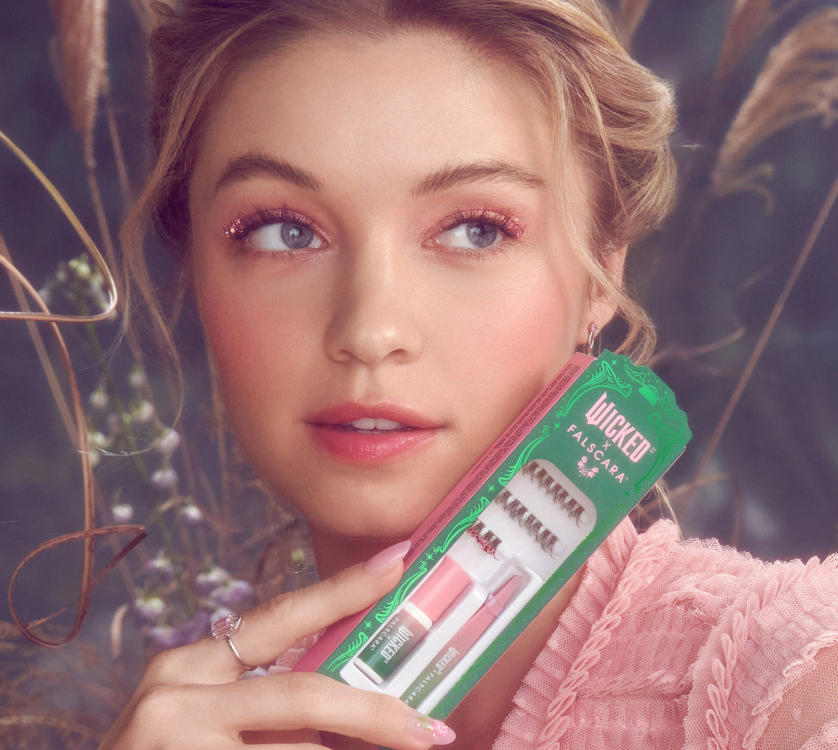 Woman holding Wicked Falscara mascara kit against botanical background.