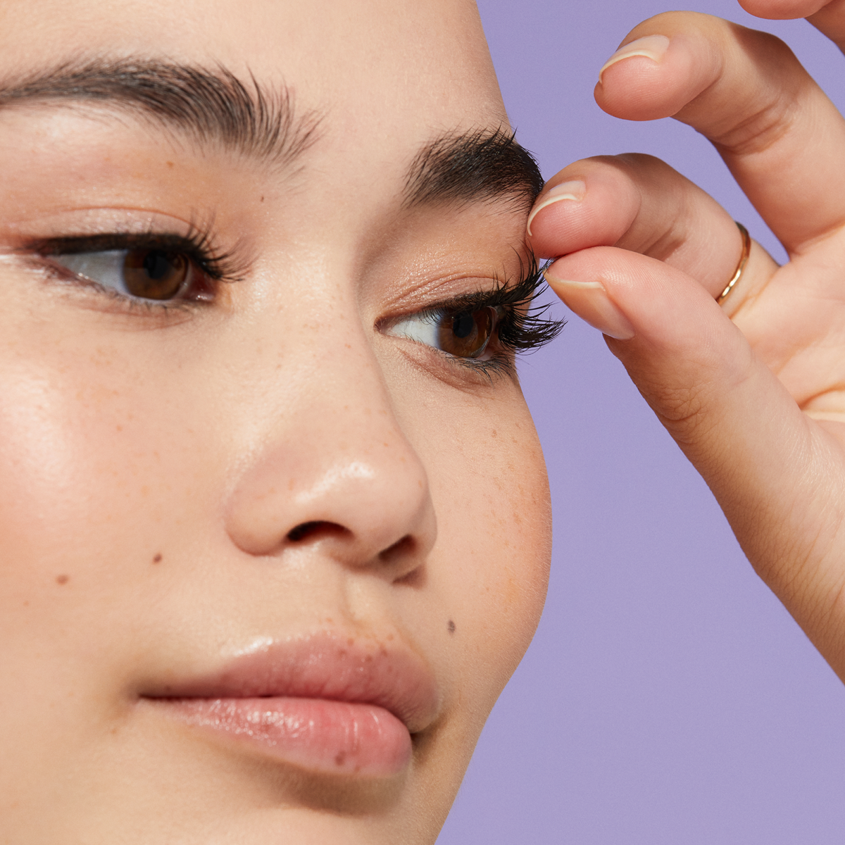 A person using their fingers to separate their natural lashes from Falscara false lashes applied underneath. 