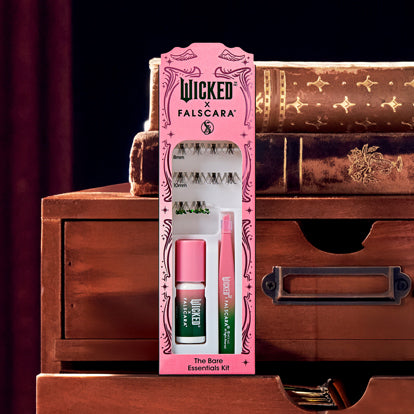 Wicked Falsçara lash essentials kit with false lashes, pink nail polish, and green mascara on wooden dresser.