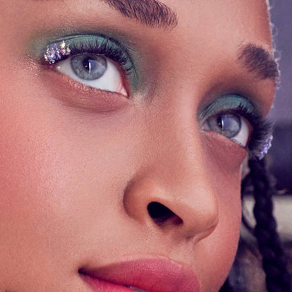 Close-up of model's face showcasing purple and blue eyeshadow with glitter.