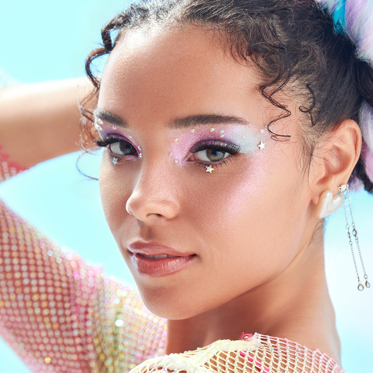 Close-up of a person with colorful makeup and hair accessories against a light blue background