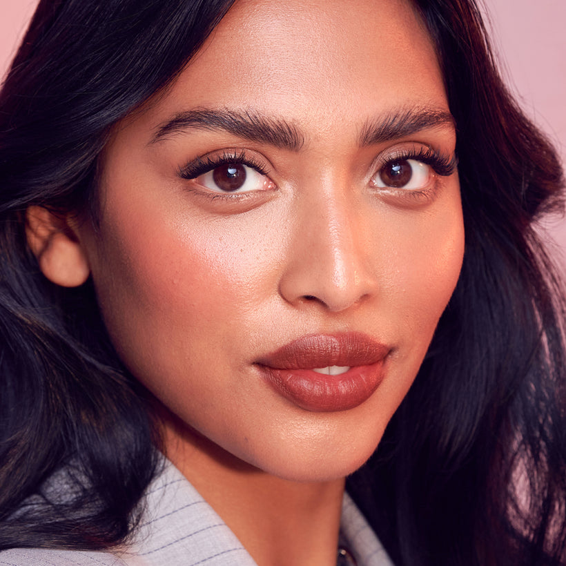Woman with dark hair and burgundy lipstick against pink background