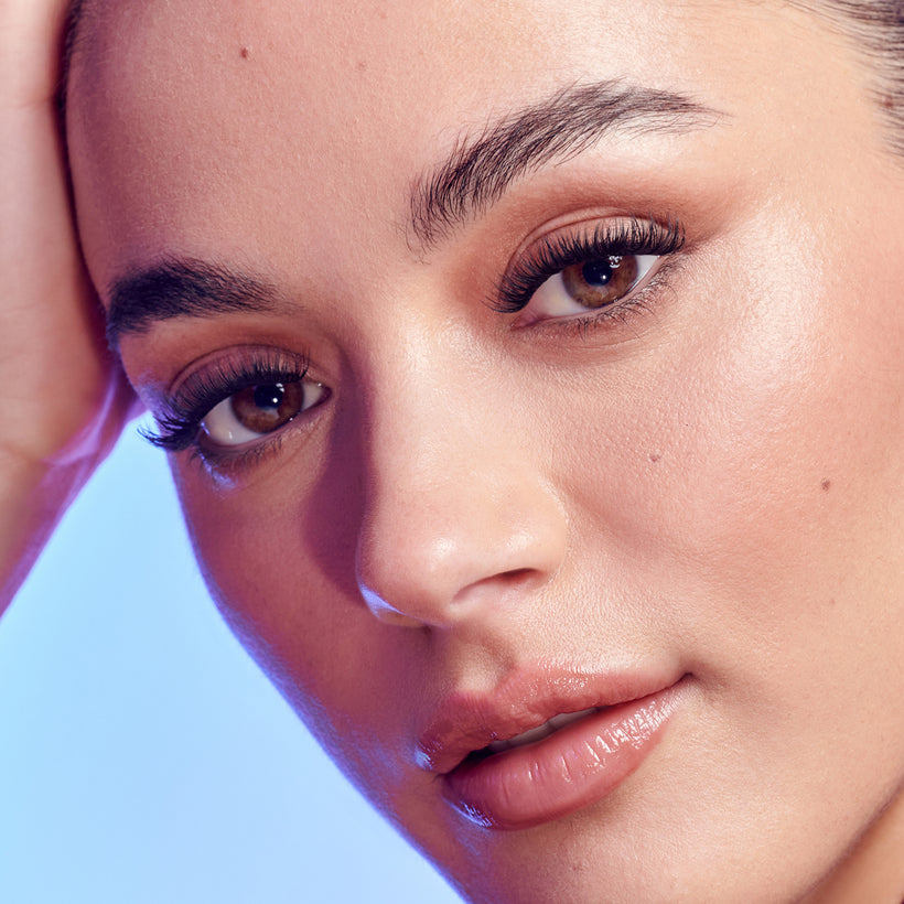 Close-up of woman's face with winged eyeliner and bold lashes against blue lighting.