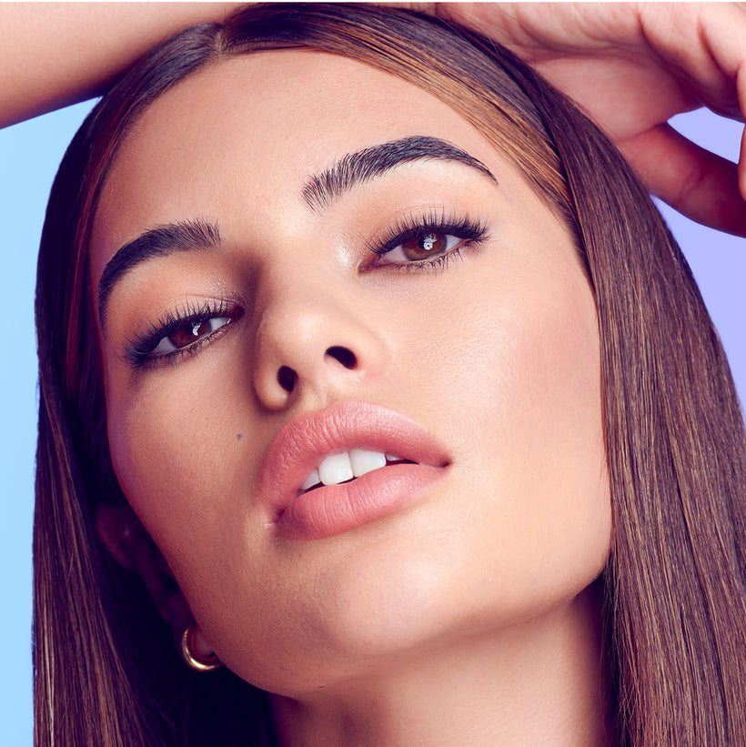 Woman with bold eyebrows and winged eyeliner looking upward against blue background