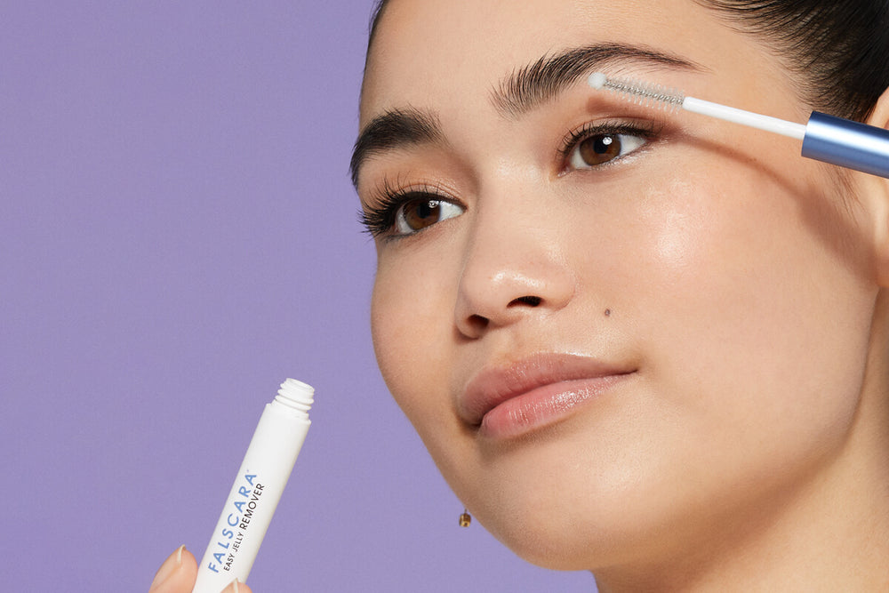 A woman applying Falscara Easy Jelly Remover to her false lashes for easy removal. The wand is shaped like a mascara wand for easy application and lash removal. 