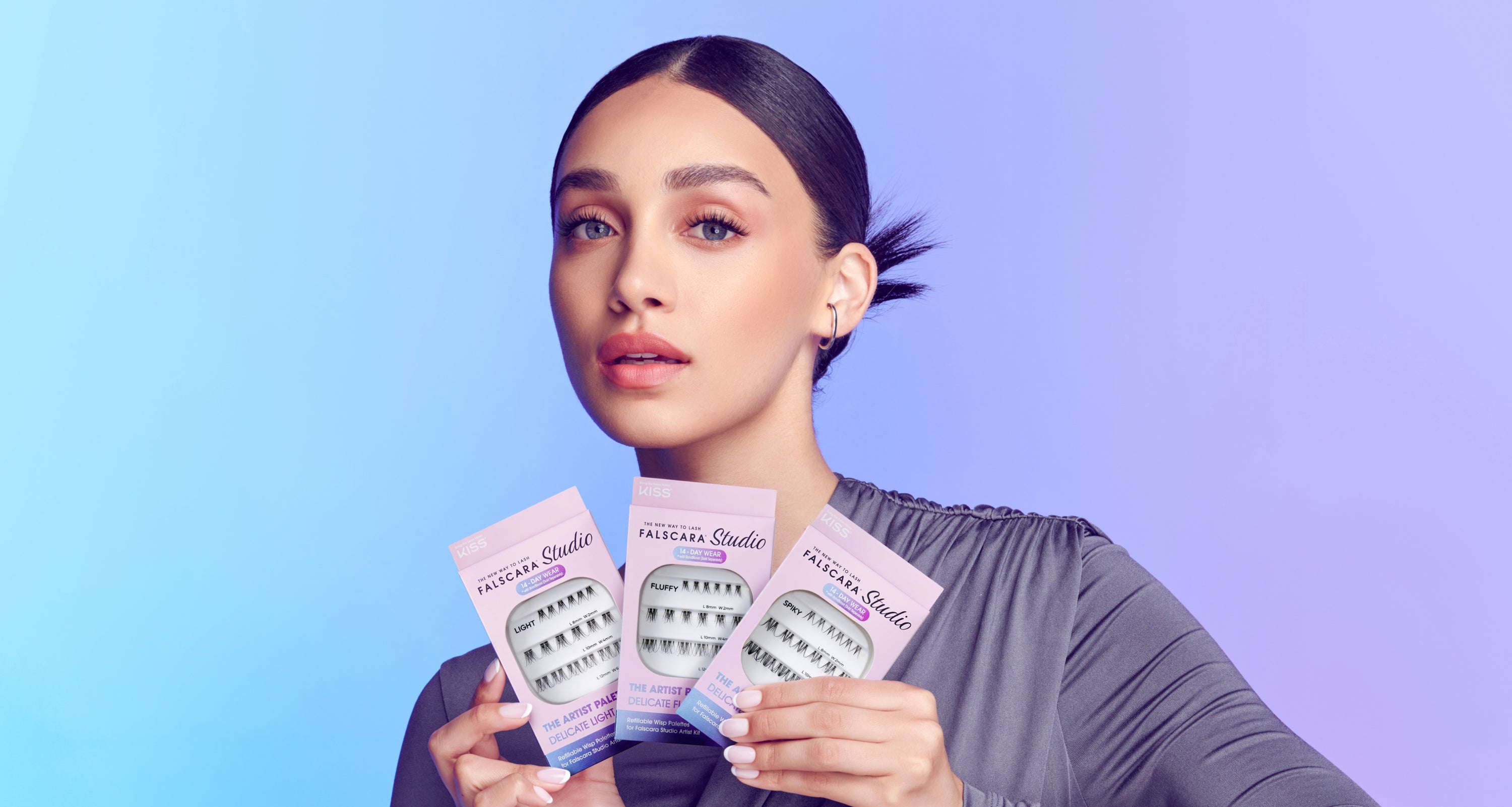 A woman wearing Falscara lashes, holding up three packages of Falscara Studio lashes in 3 different styles. 