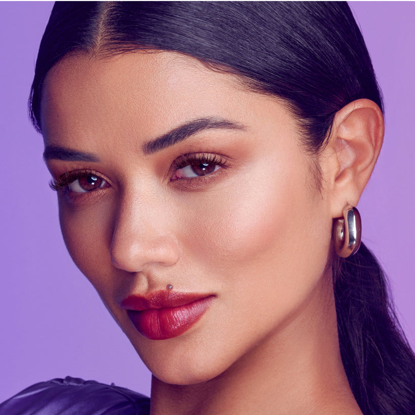 Woman wearing dark chocolate fluffy lashes against purple background, modeling Falscara lash product.