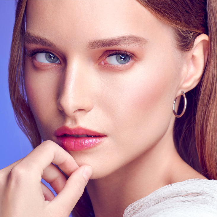 Woman modeling Falscara Studio Petite Dainty Collection lashes with pink lipstick against blue background.