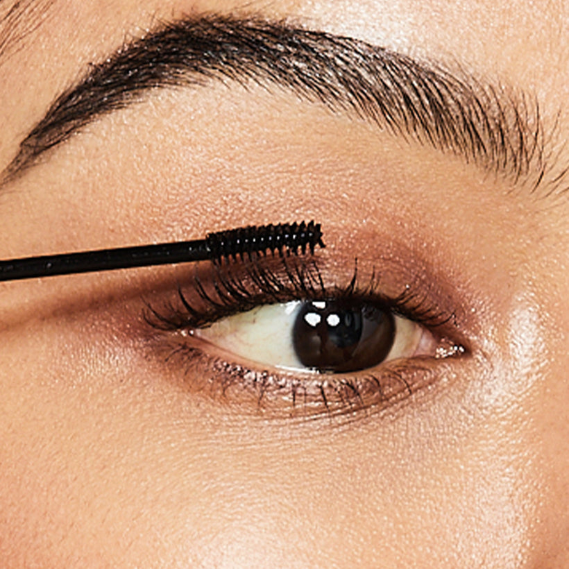 Mascara brush applying black mascara to upper lashes on open eye