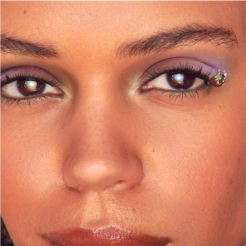 Close-up of woman's face wearing purple eyeshadow and false lashes with jeweled accent.