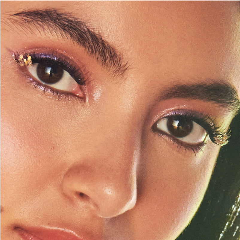 Close-up of model's face showcasing dramatic eye makeup with gold accents and winged eyeliner.