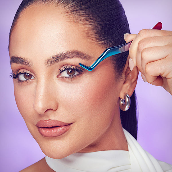A woman modeling beautiful, long, full lashes from Falscara, holding up the lash applicator she used to easily apply the false lashes. 